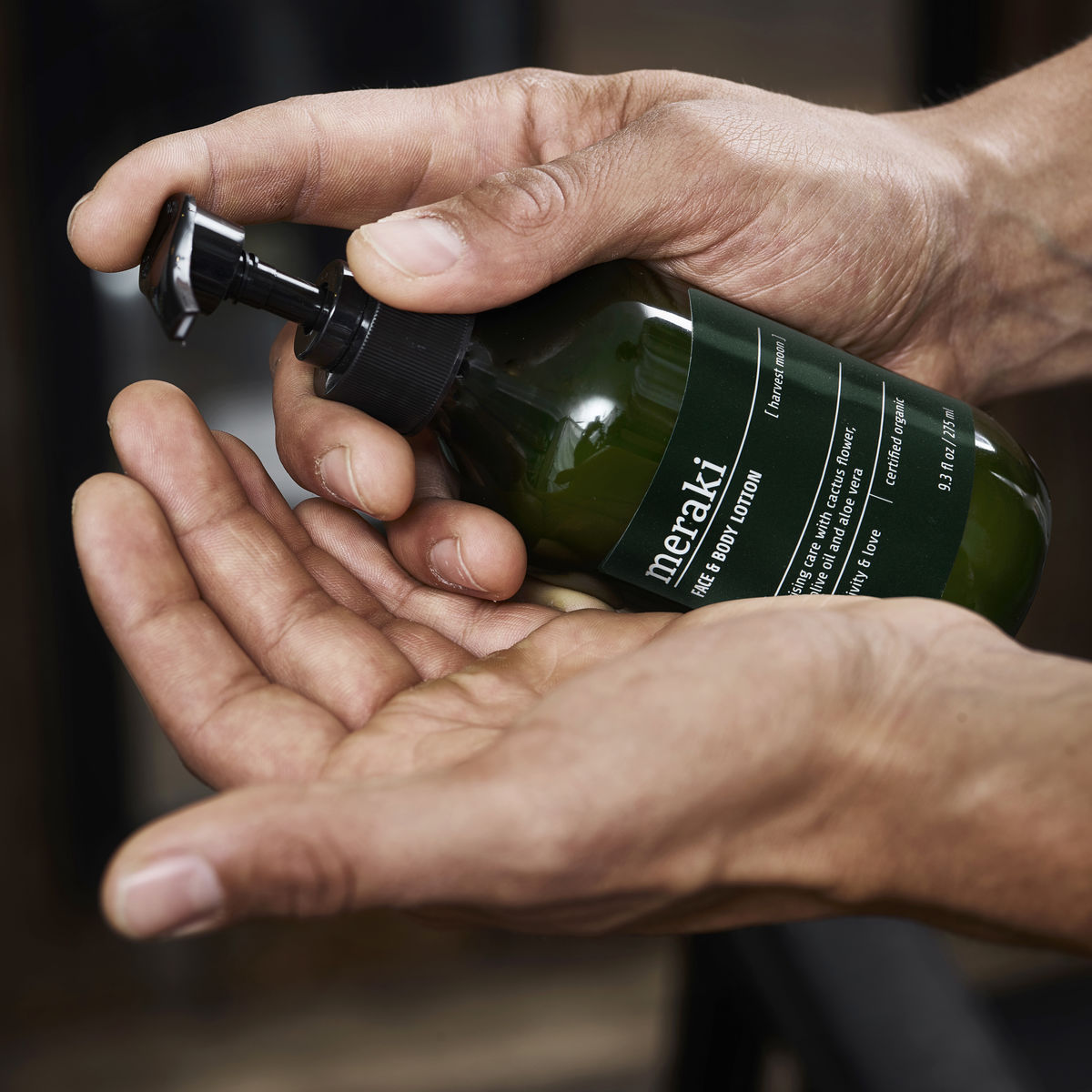 A dark green bottle with black pump and a label that says 'Meraki Face & Body Lotion'
