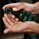 A dark green bottle with black pump and a label that says 'Meraki Face & Body Lotion'